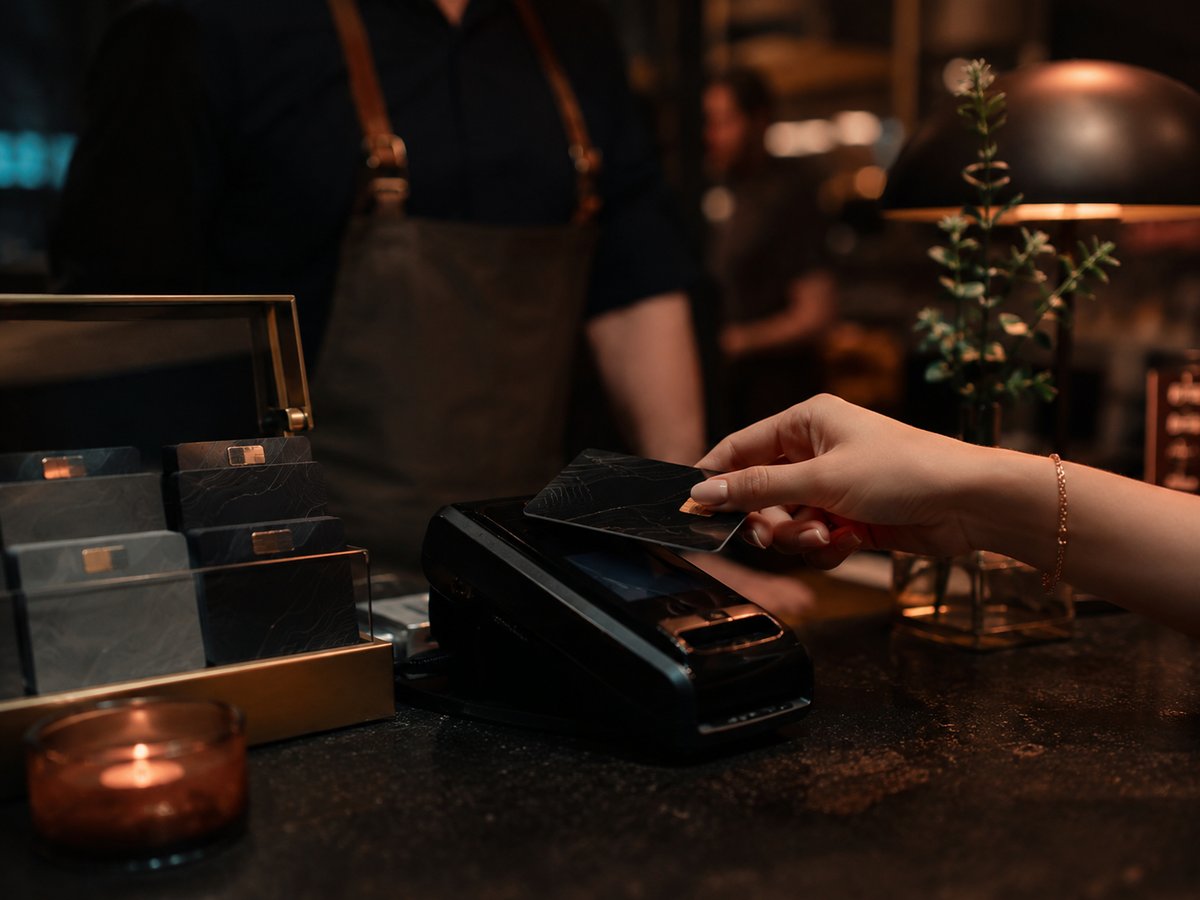 A guest tapping a branded loyalty card at a restaurant counter, gift cards displayed nearby